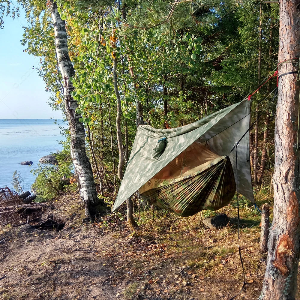 The Ultimate Outdoor Adventure Hammock Shelter System fully set up and suspended between two trees outdoors, positioned by the seaside.